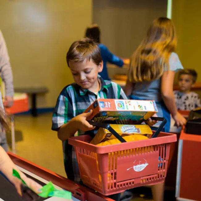 A young boy holding a shopping basket filled with fake groceries