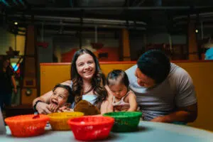 a woman and child laugh and pose while sitting next to a man watching his toddler draw at a table the Discovery Children's Museum