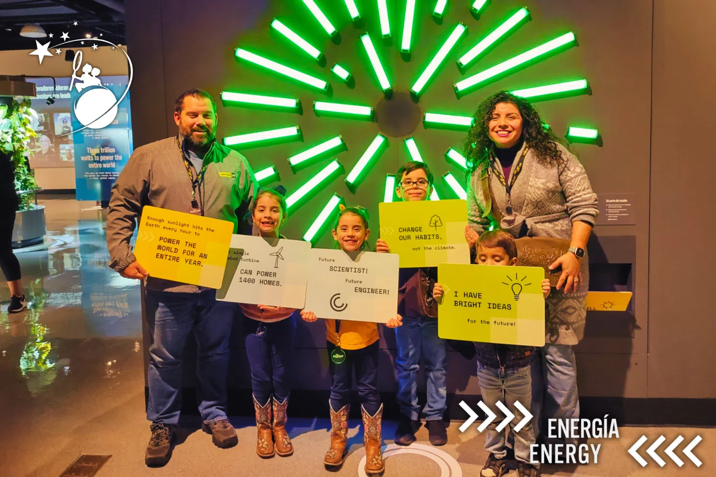 2 parents and 4 children pose for a photo and hold signs with facts and slogans written on them at the Discovery Children's Museum