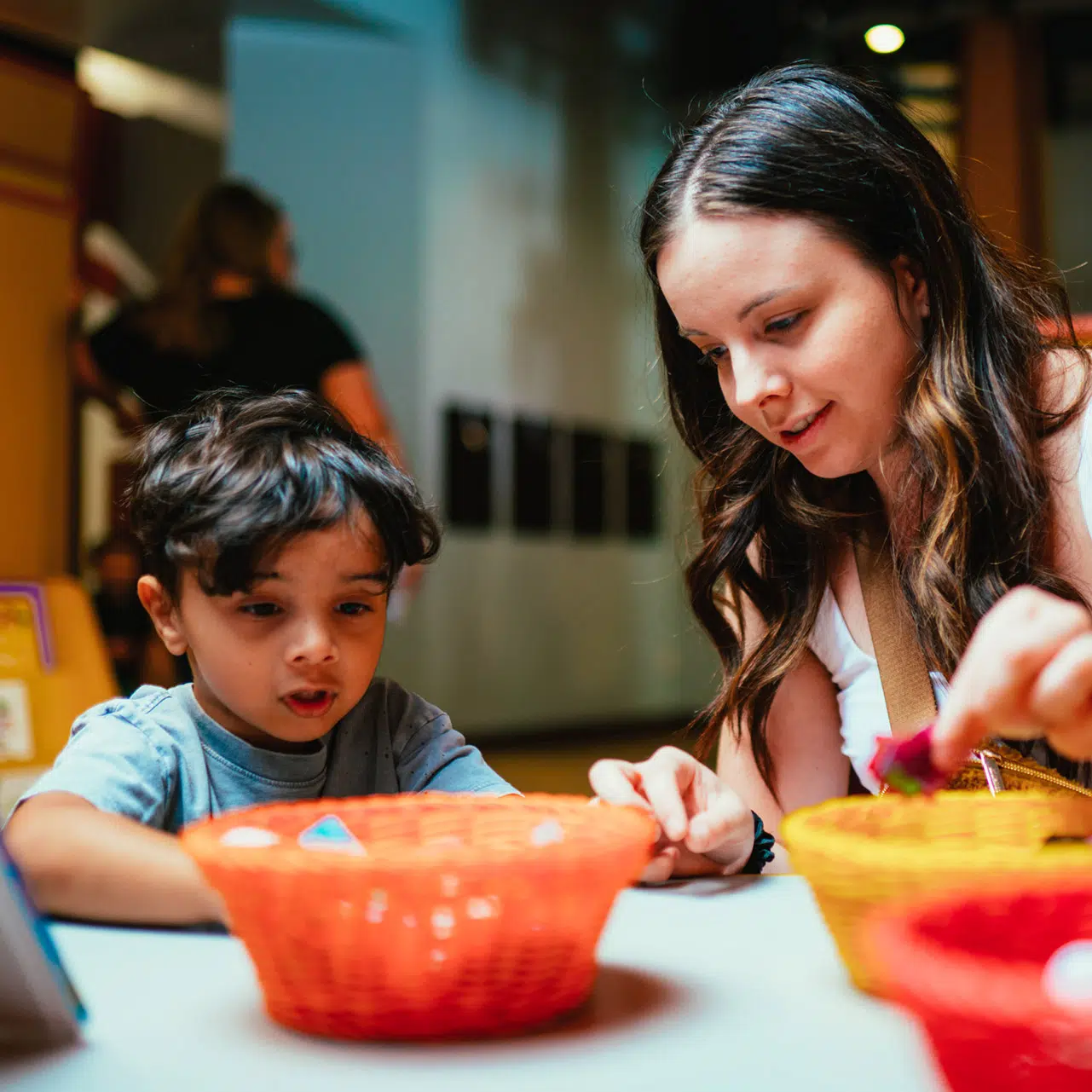 woman sitting next to her young child near colored baskets of craft supplies Discovery Children's Museum