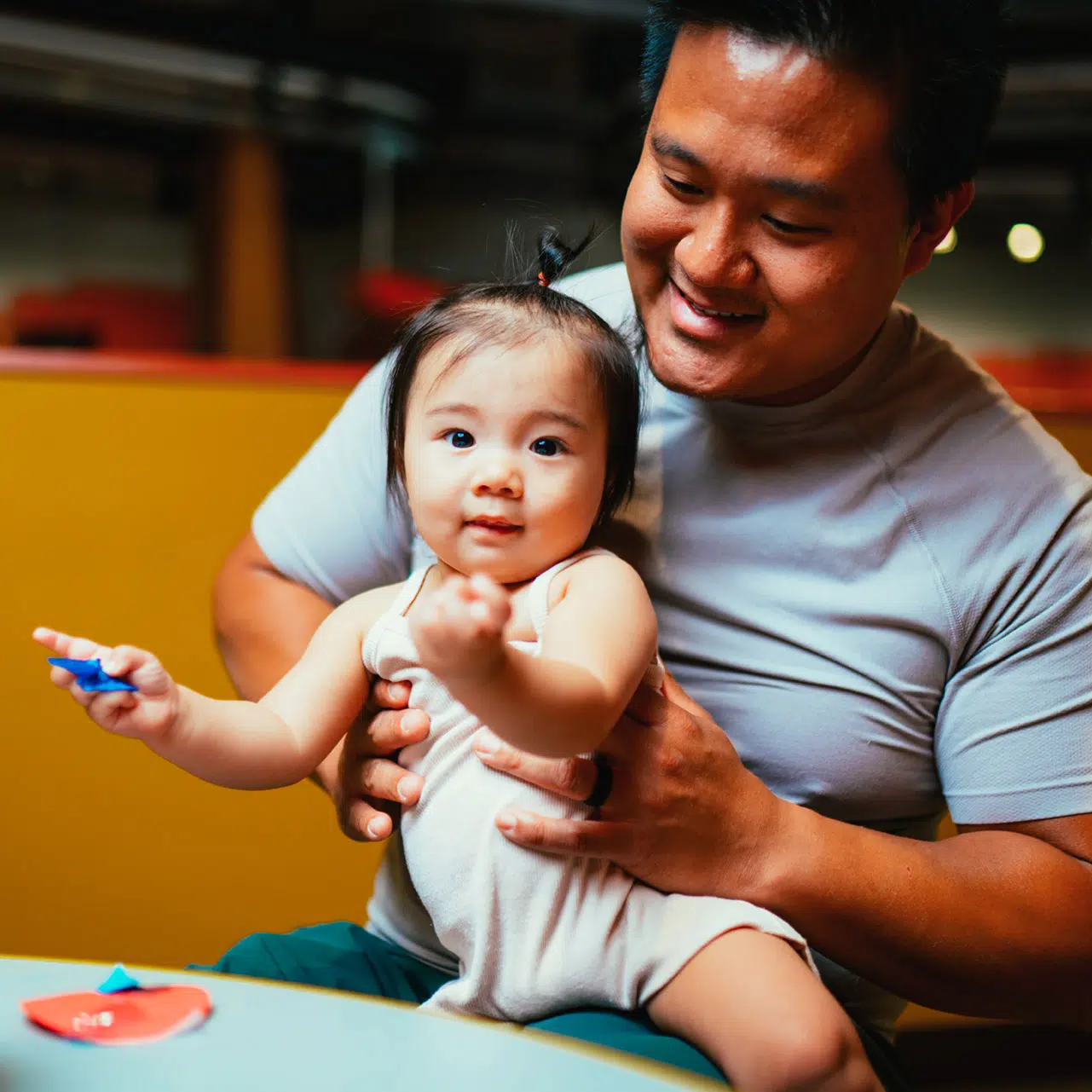 A father holds his toddler daughter while she holds paper crafts at the Discovery Children's Museum