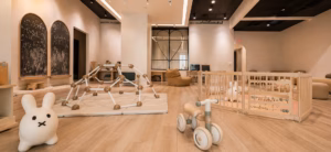 "Interior of WonderPlay Cafe, a children's play space featuring a climbing structure, balance bike, bunny plush toys, a gated infant play area, chalkboard wall art, and warm wood flooring throughout." 