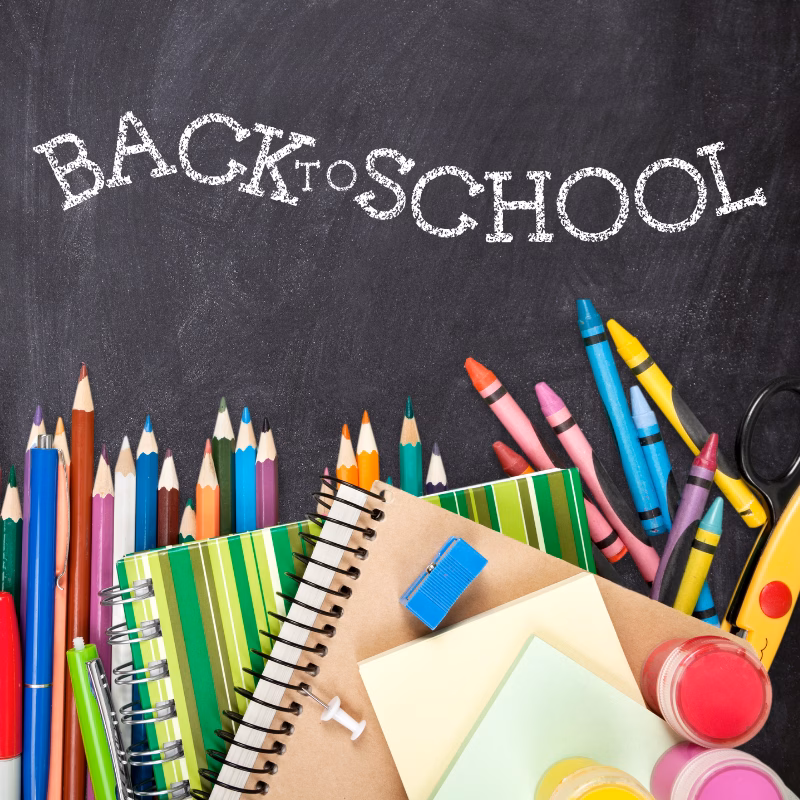 BACK TO SCHOOL Promotional graphic for Back to School at DISCOVERY Children's Museum featuring colorful school supplies including colored pencils, crayons, notebooks, and scissors arranged against a chalkboard background.